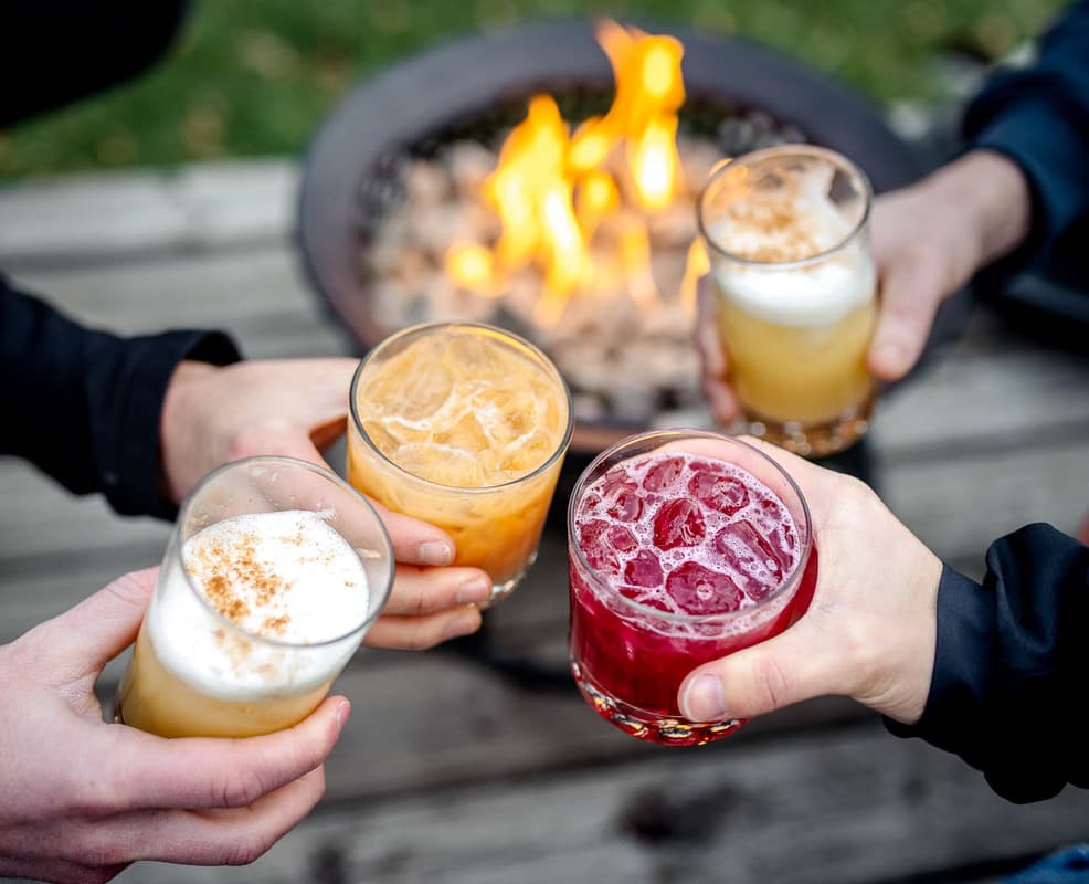Four people toasting with cocktails around an outdoor fire pit